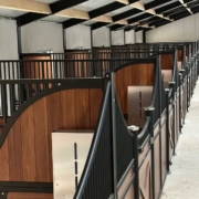 Stallgasse mit 45 zeitgesteuerten Kraftfutterautomaten des Powerfeeder-Systems Stallgasse mit mehreren Pferdeboxen aus Holz und Metall, an jeder Box ein Edelstahl-Kraftfutterautomat installiert.